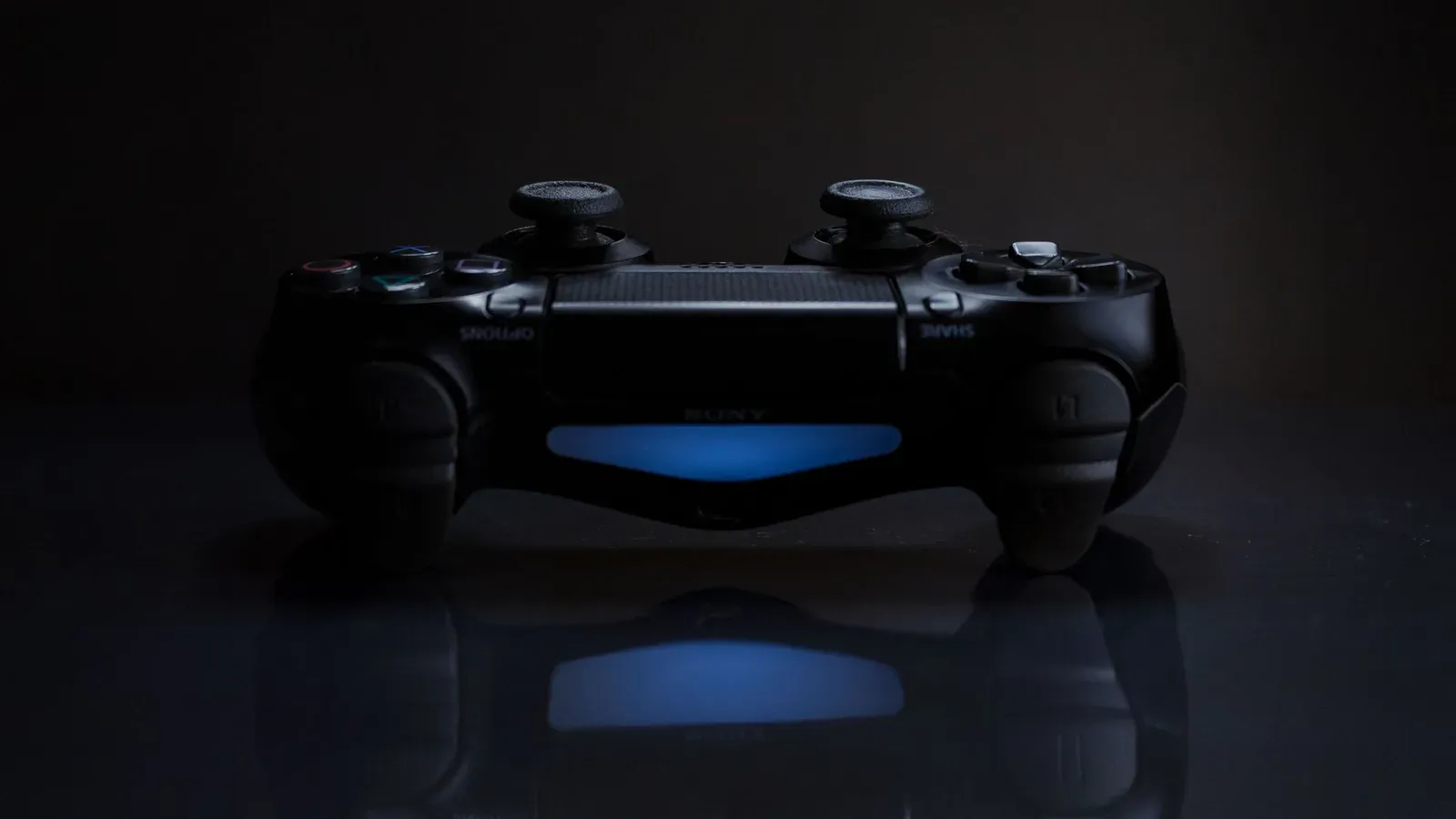 Close-up of a gaming controller with a soft blue light in a dark setting.