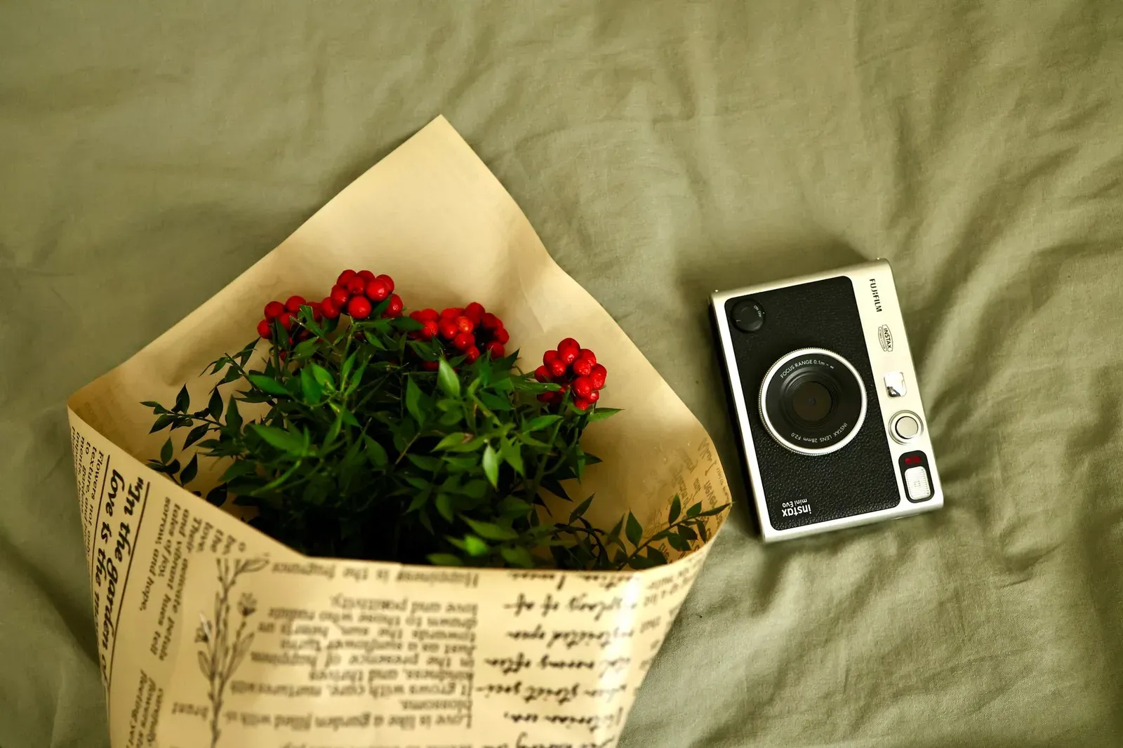 A vintage camera next to a flower bouquet with red berries on a green fabric background.
