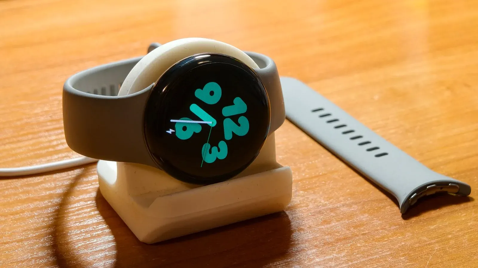 Smartwatch charging with a digital time display, extra strap nearby.