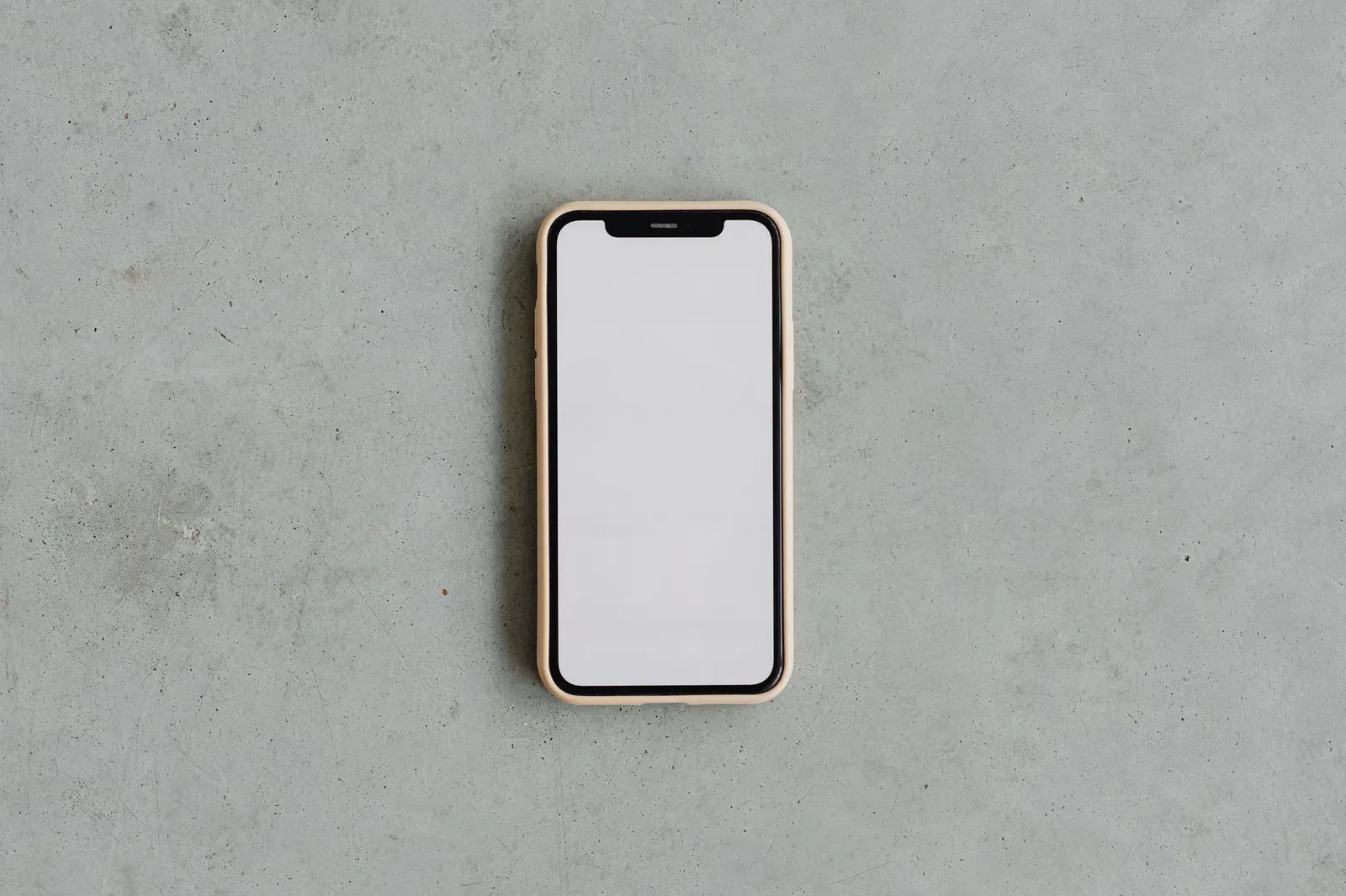 Top view of a modern smartphone with a blank white screen on a gray concrete background, ideal for mockups.